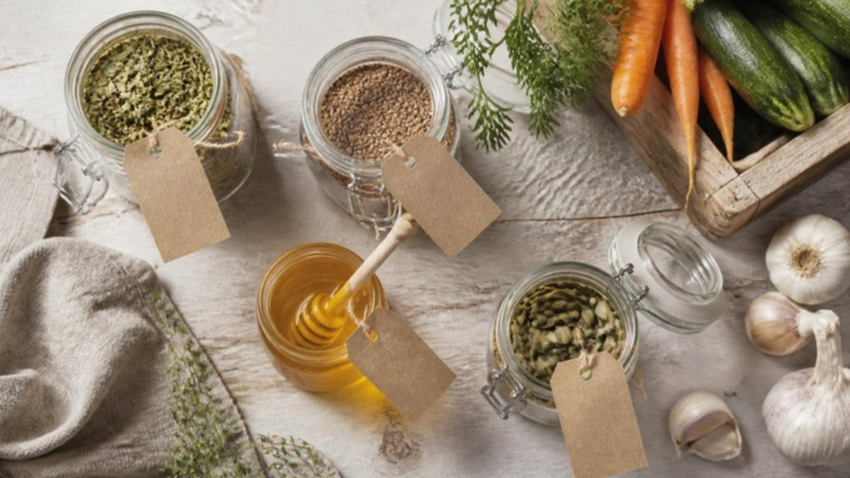 Gläser mit naturbelassenen Lebensmitteln und leeren Papieretiketten neben frischem Gemüse auf einem Holztisch