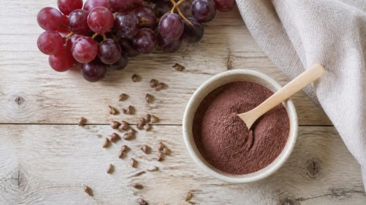 Rote Trauben, Traubenkerne und eine Schale mit rötlich-braunem Traubenkernpulver auf einem Holztisch