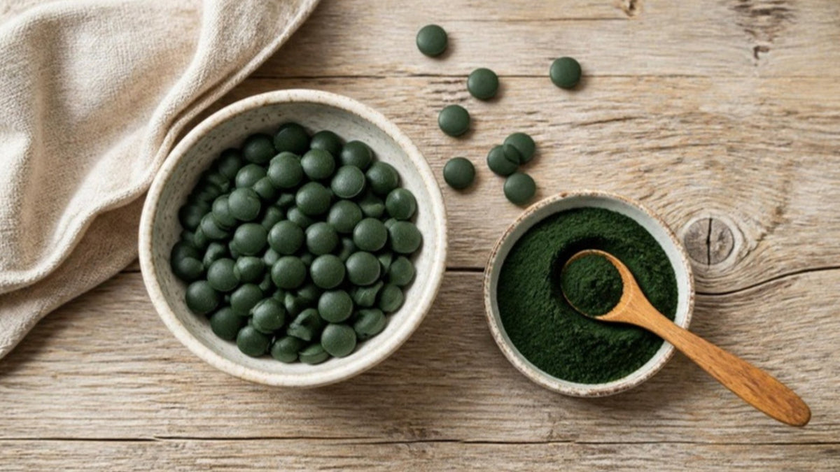 Dunkelgrüne Chlorella-Presslinge in einer Schale neben einem Schälchen mit grünem Algenpulver auf einem Holztisch